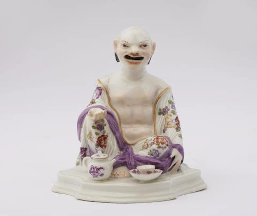 A Meissen porcelain figure of a seated Budai with tea implements