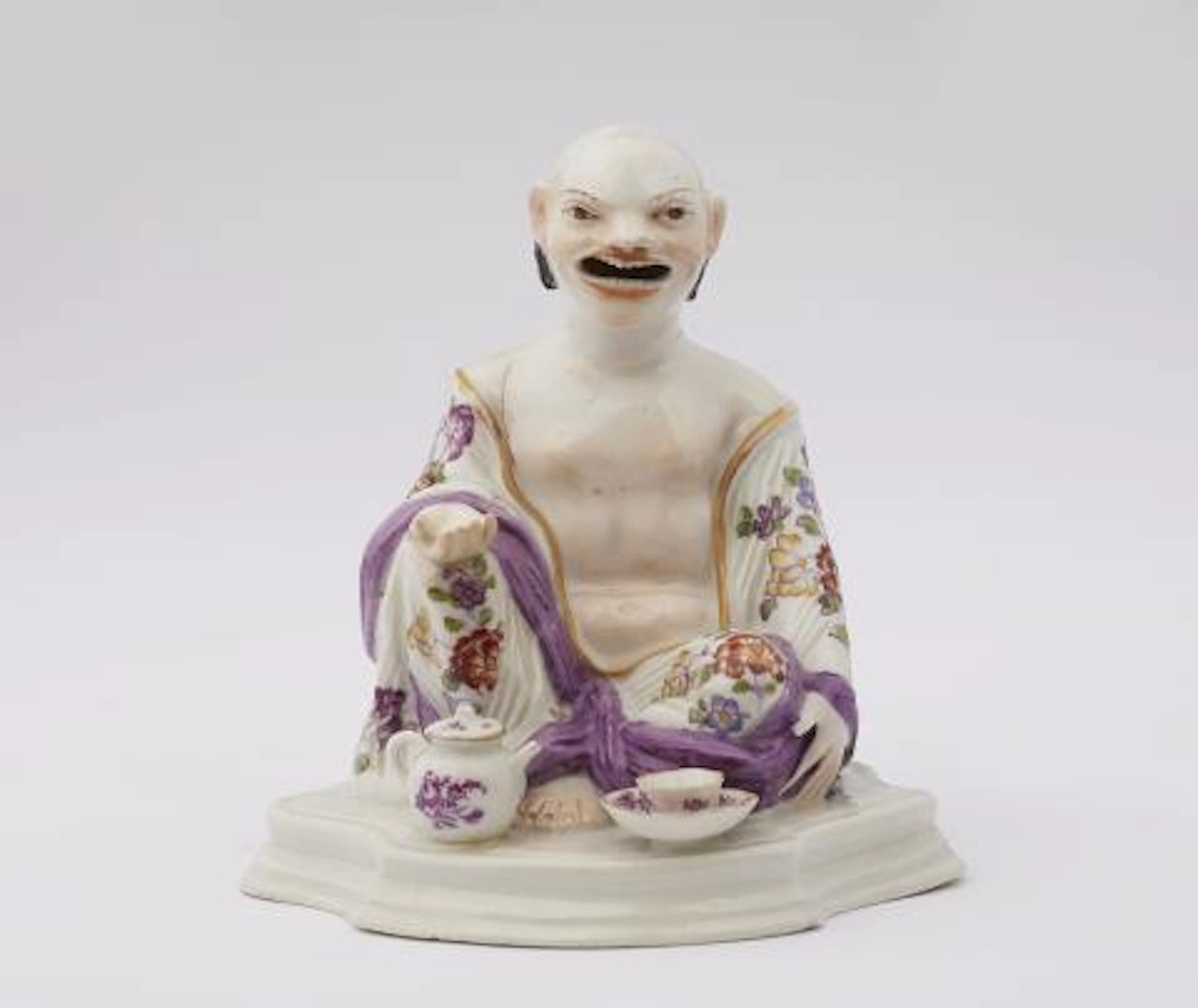 A Meissen porcelain figure of a seated Budai with tea implements