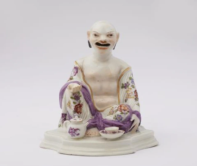 A Meissen porcelain figure of a seated Budai with tea implements