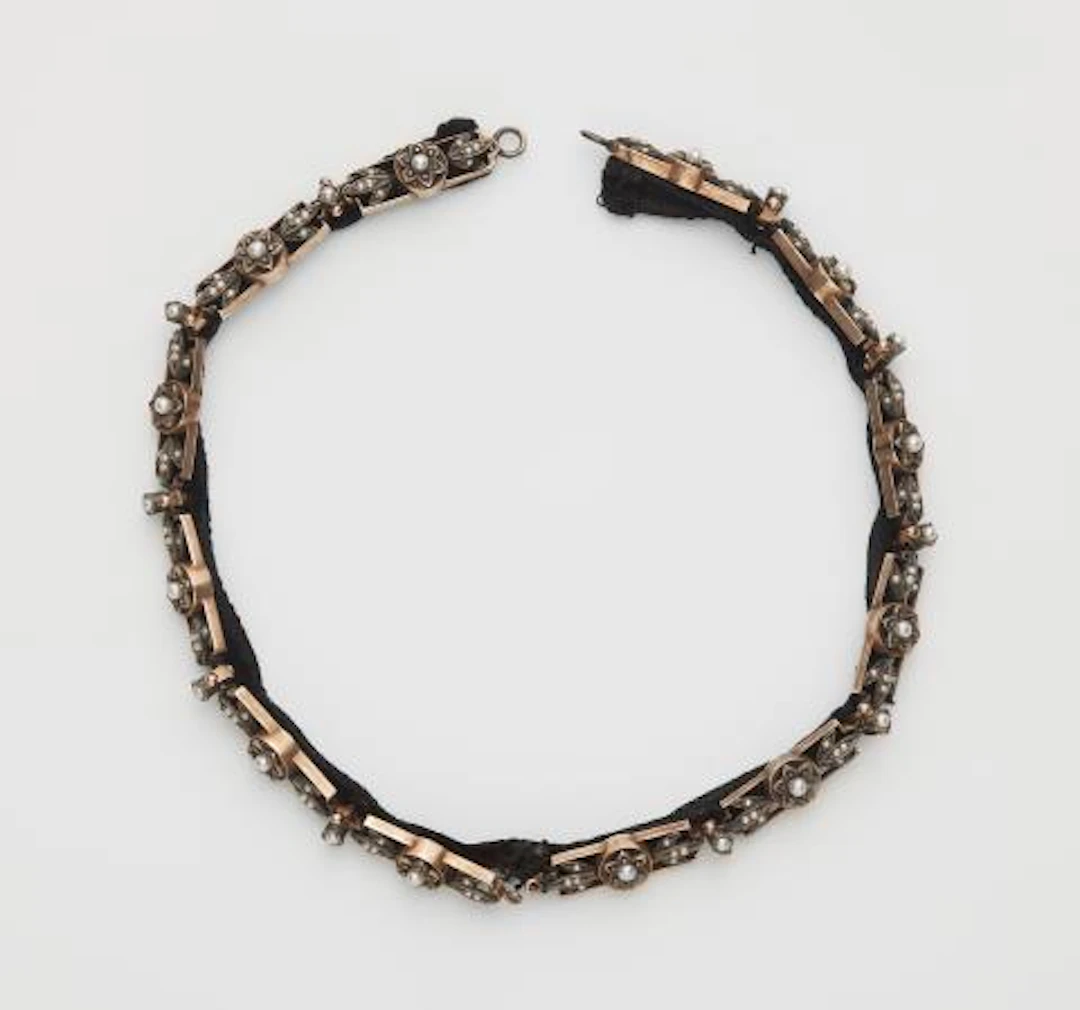 A velvet band with sewn on gilded silver and pearl relief decoration.