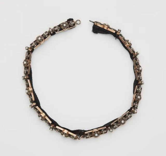 A velvet band with sewn on gilded silver and pearl relief decoration.
