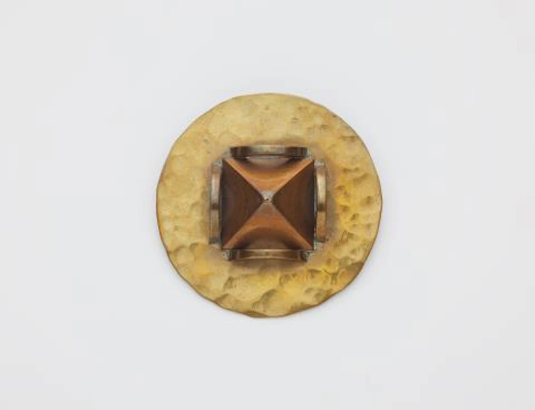 A French hammered brass and copper disc brooch with pyramidal motif.