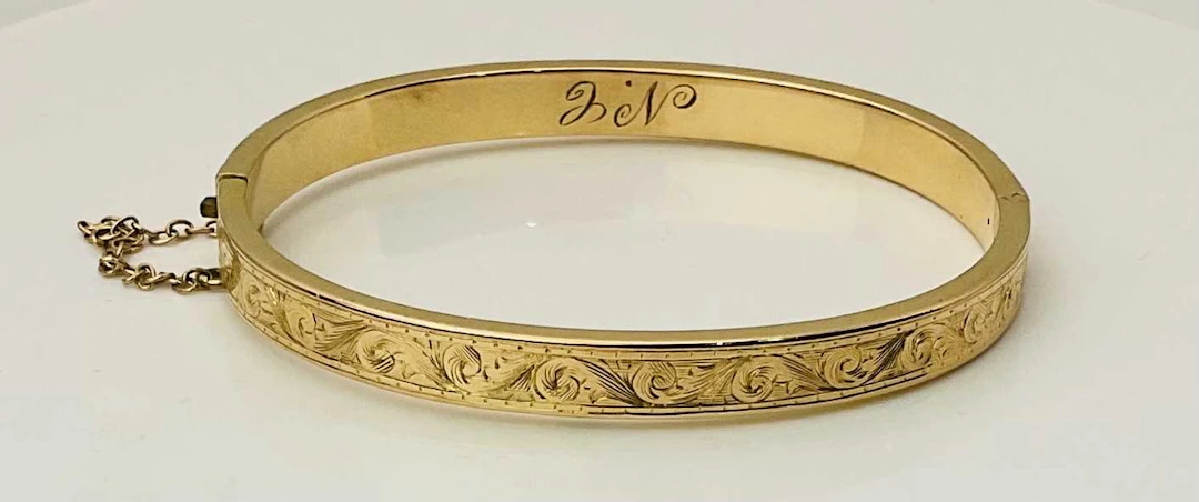 A yellow metal hinged snap bangle with bright cut floral decoration