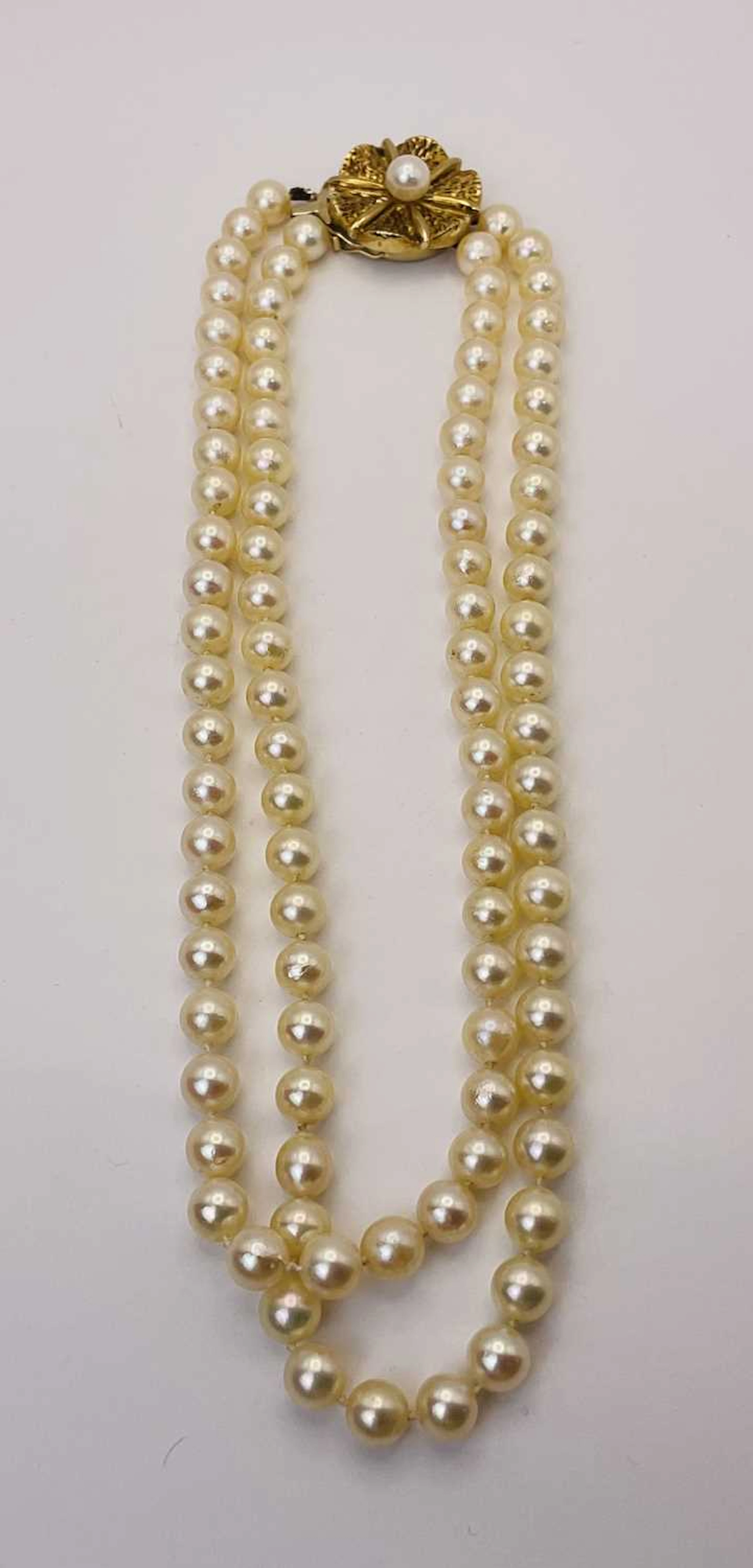 A boxed set of single strand pearls with ornate circular...