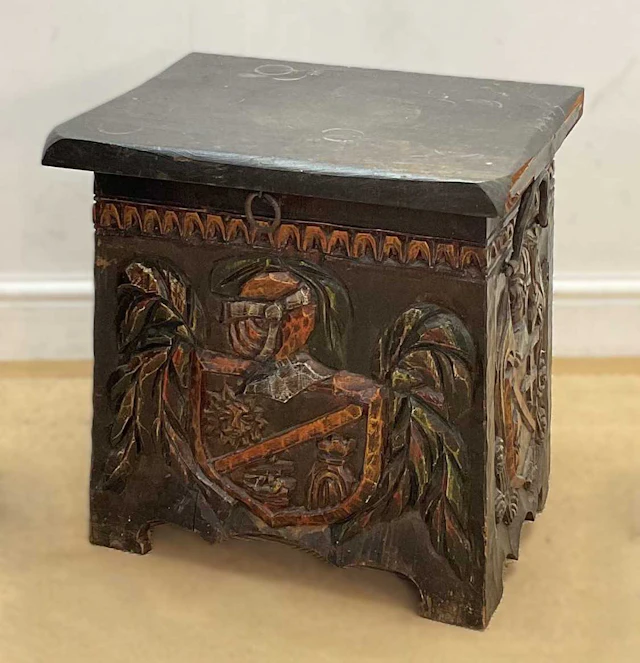 A stained wooden coal box with carved coat of arms to the front