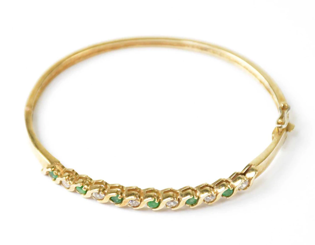 A 9ct yellow gold hinged bangle set with alternating green and white stones