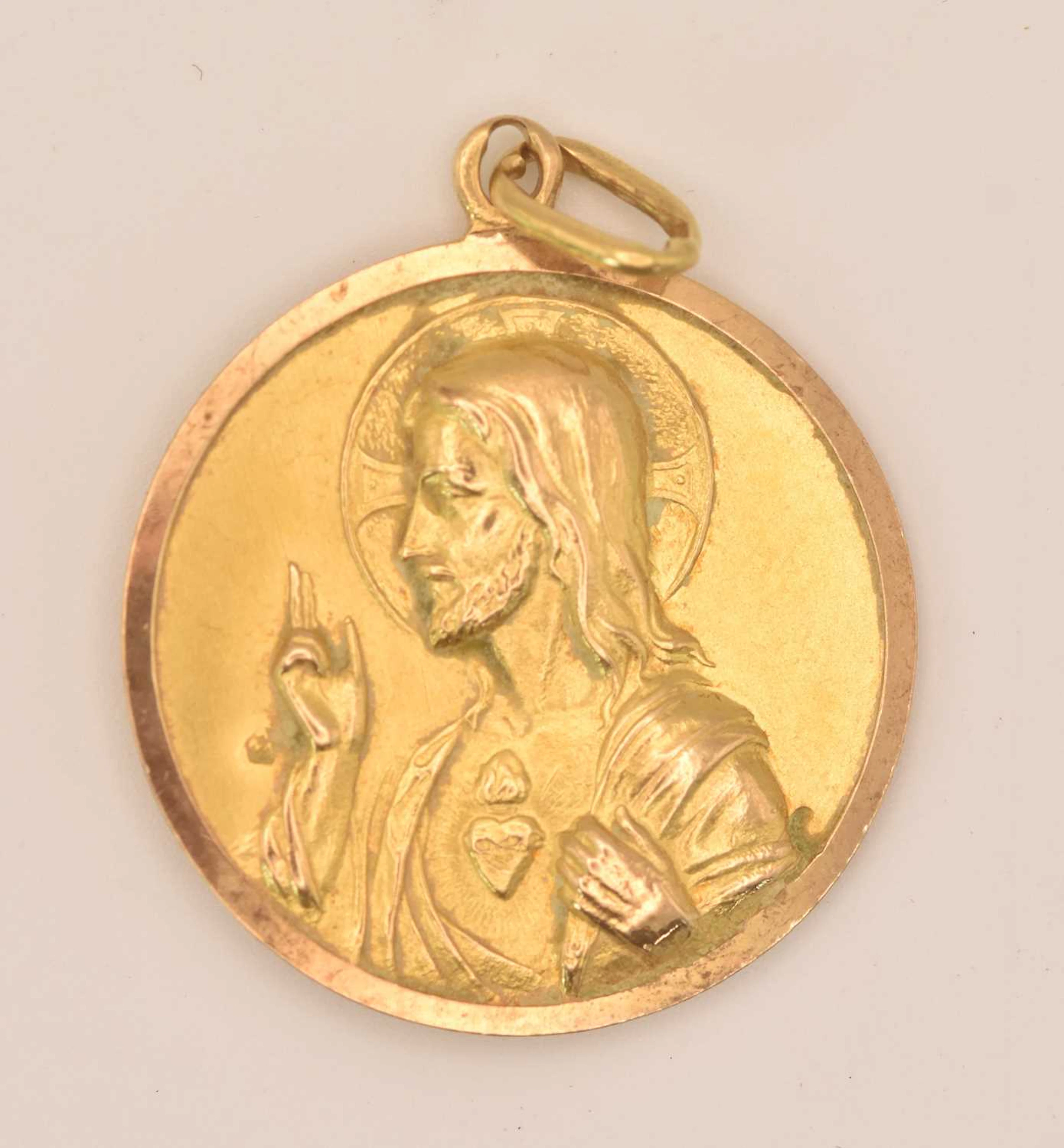 A circular yellow metal pendant depicting Jesus Christ