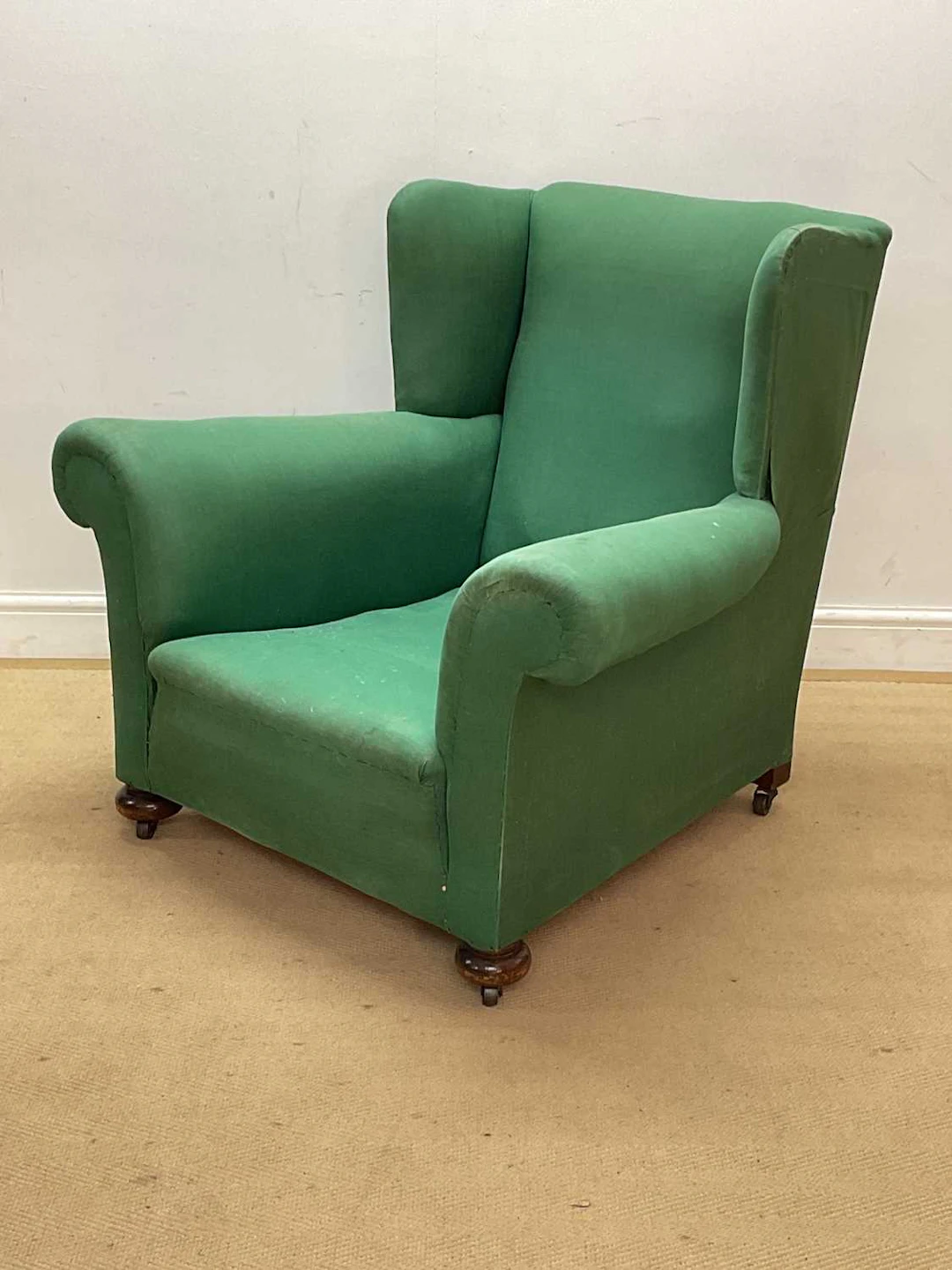 A green upholstered armchair on bun feet and castors