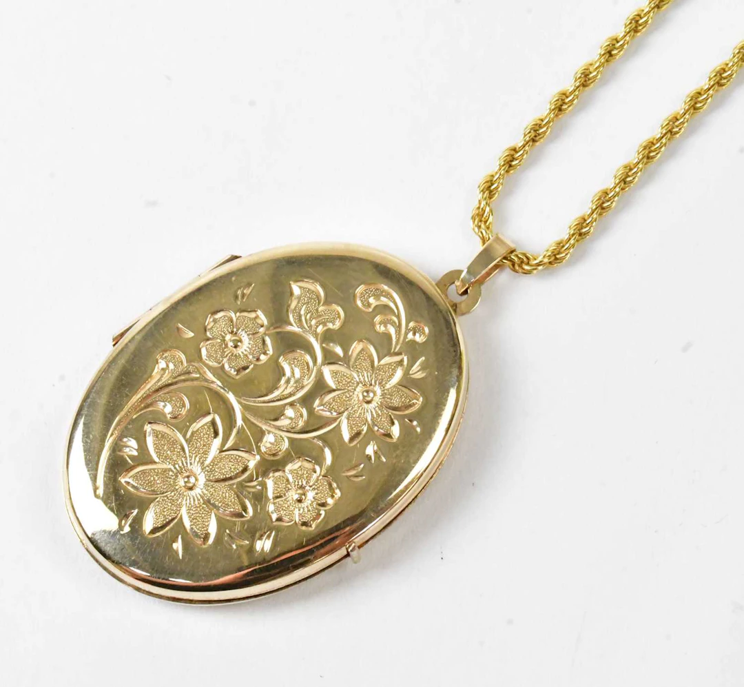 A 9ct yellow gold oval locket with floral engraving to...