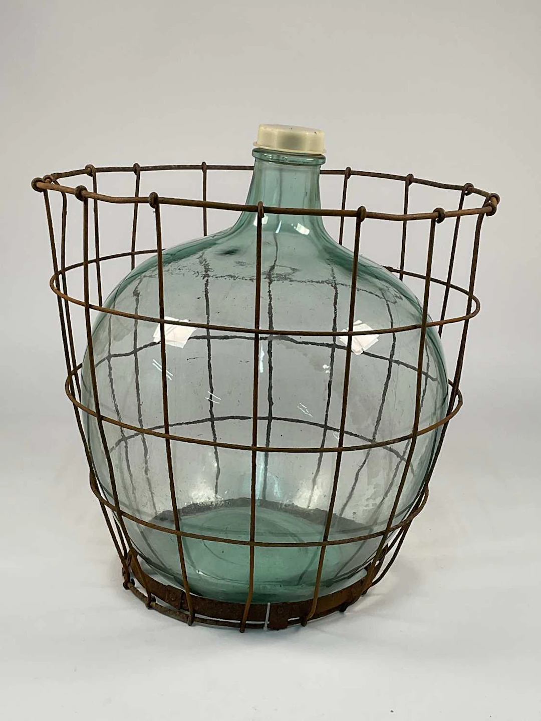 A vintage green glass carboy enclosed within a metal wire cage