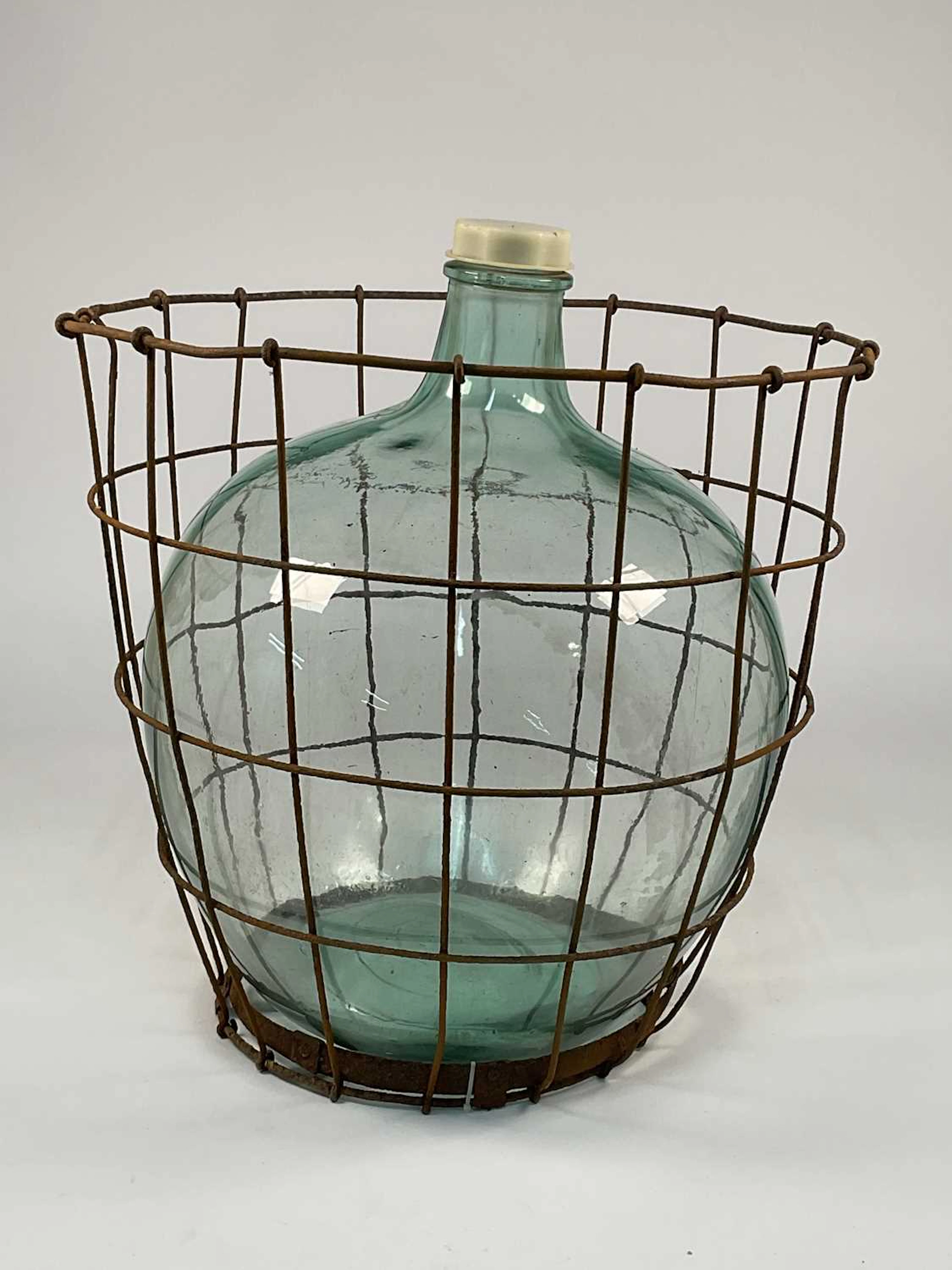 A vintage green glass carboy enclosed within a metal wire cage