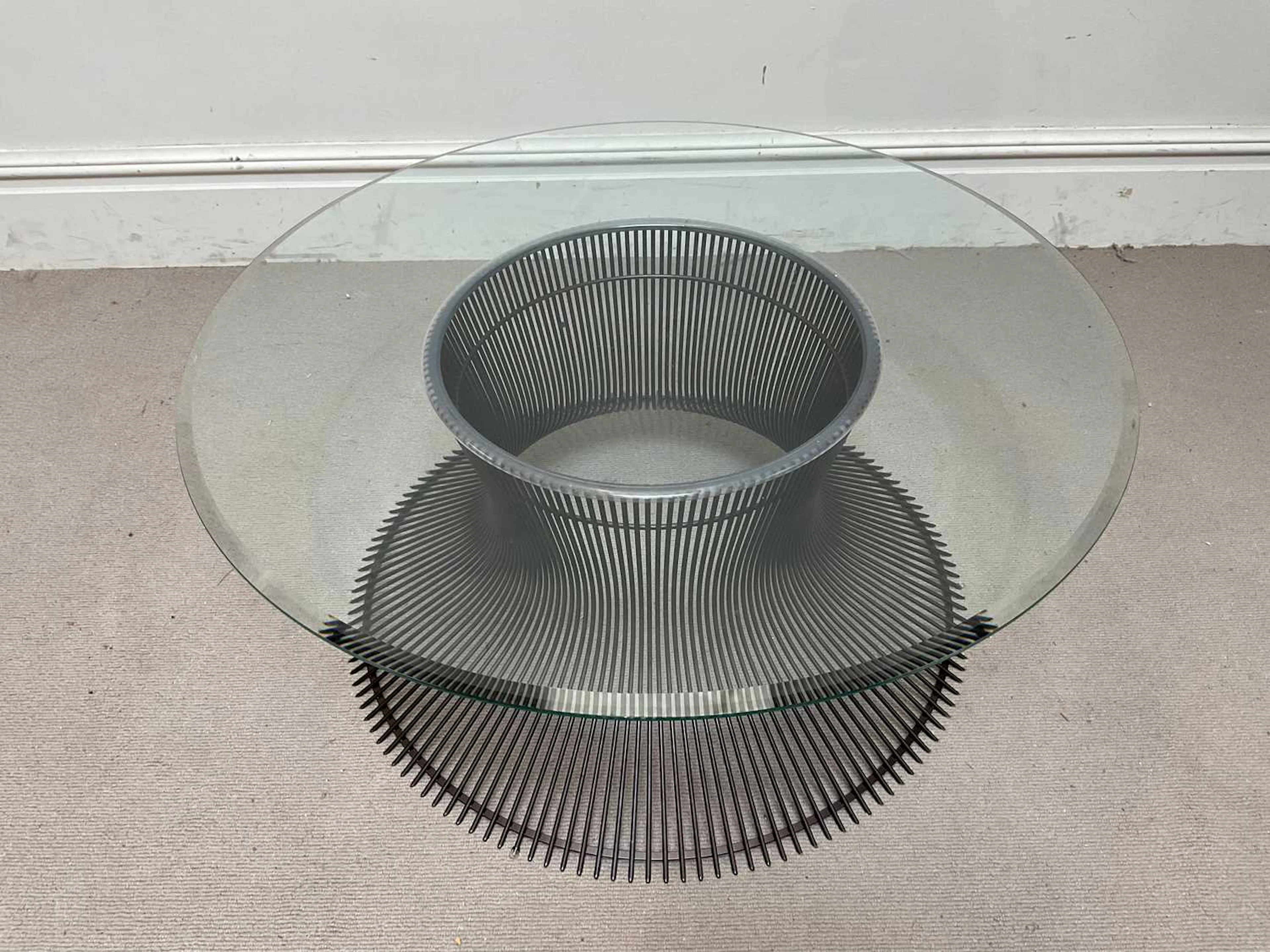 A contemporary coffee table with thick circular glass top on black wire base