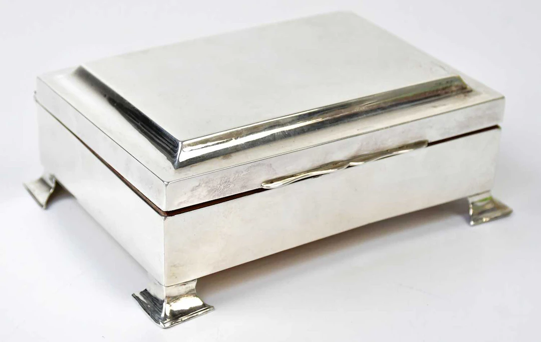 A silver wooden lined cigarette box raised on bracket feet