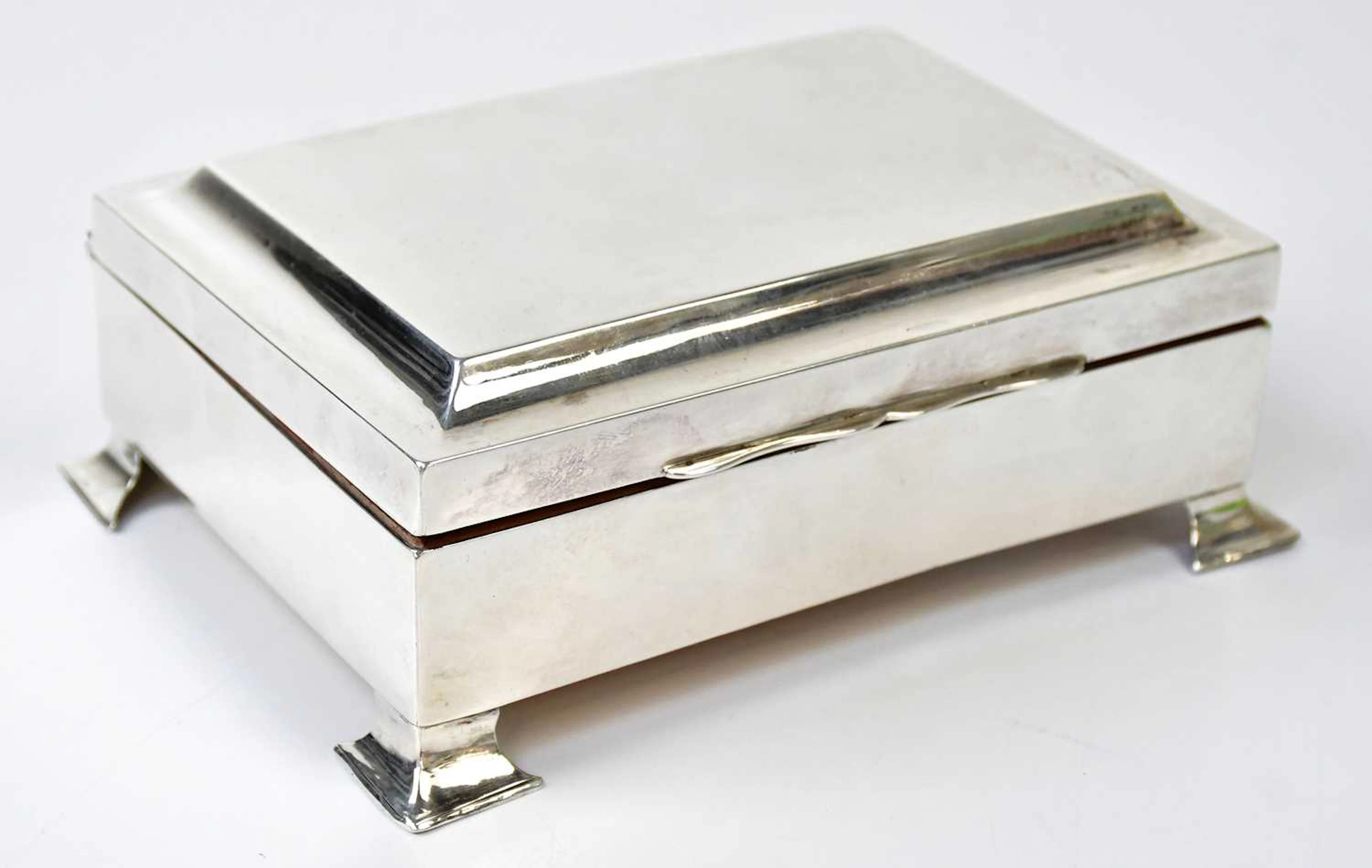 A silver wooden lined cigarette box raised on bracket feet