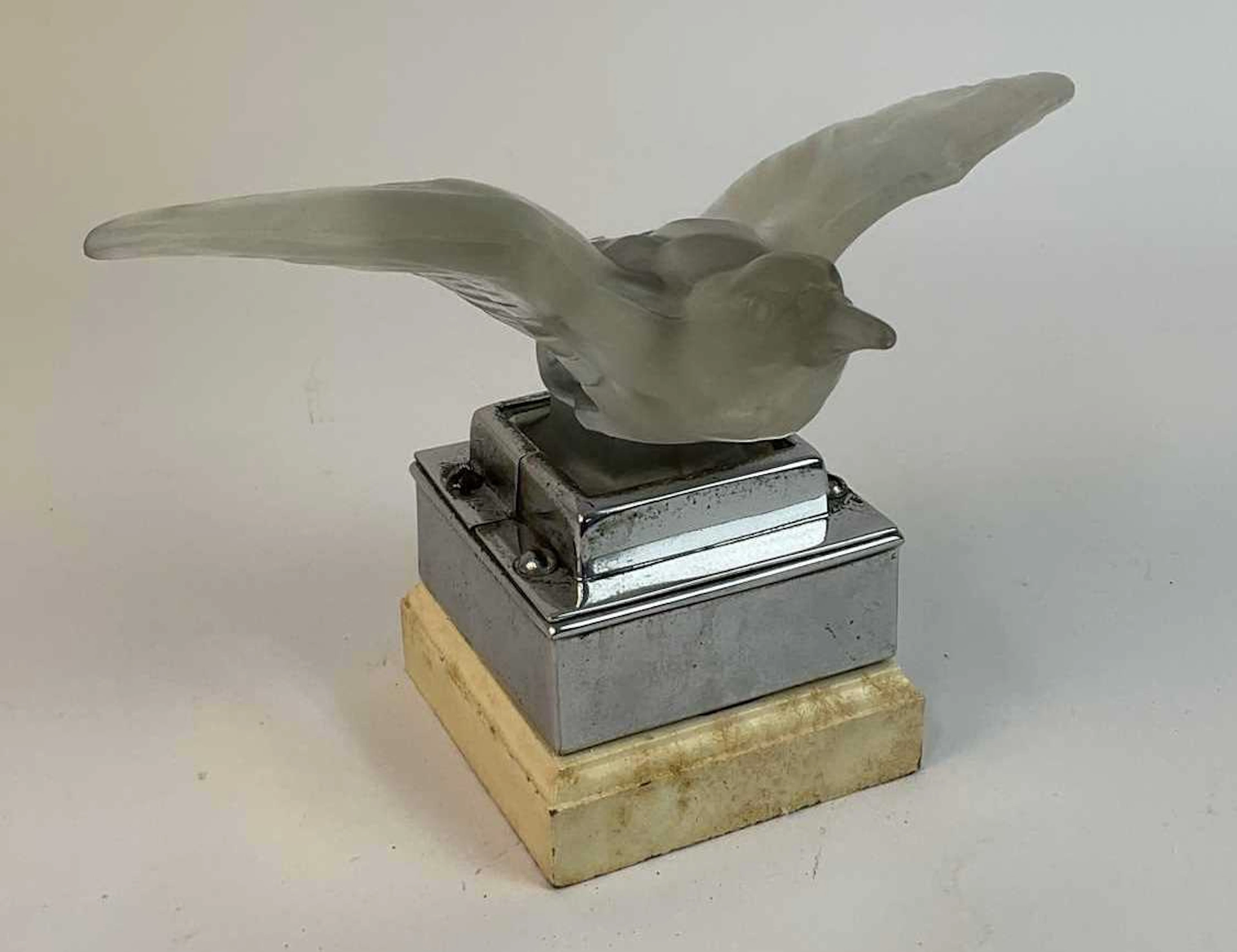 A glass bird hood ornament mounted on a chrome and wooden plinth