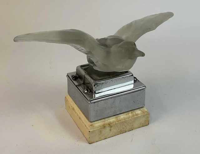 A glass bird hood ornament / car mascot mounted on a chrome and wooden plinth