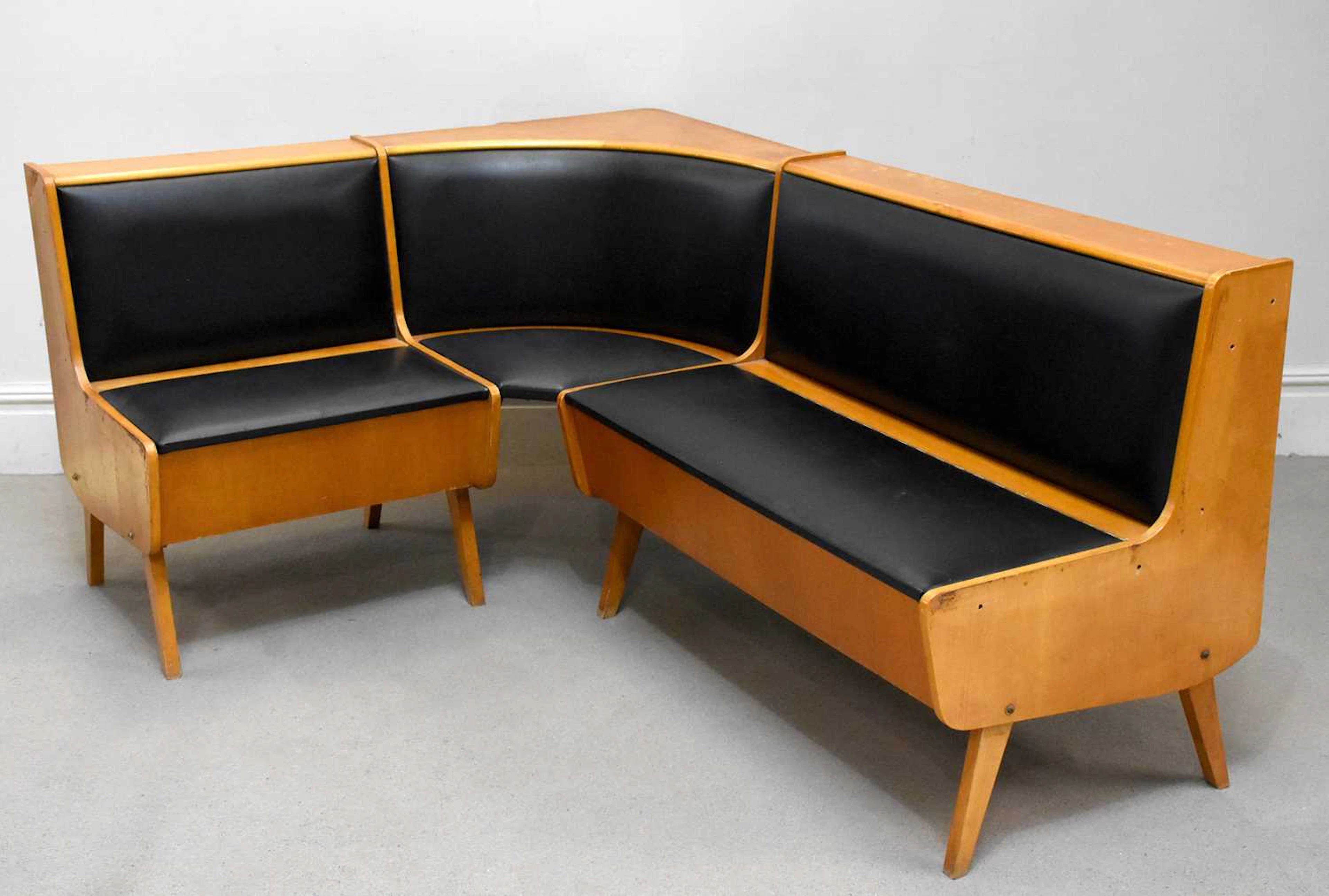 A retro teak corner lounge suite upholstered in a black vinyl material
