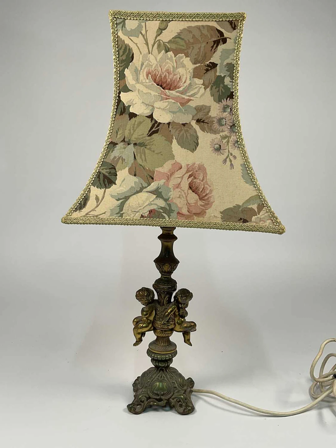 A decorative brass table lamp with two cherubs on a scrolled base