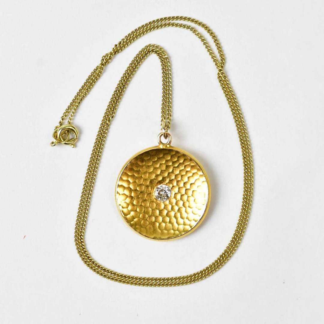 A yellow metal circular pendant set with a central diamond