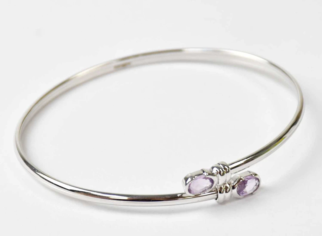 A 9ct white gold torc bangle set with an oval amethyst to each end
