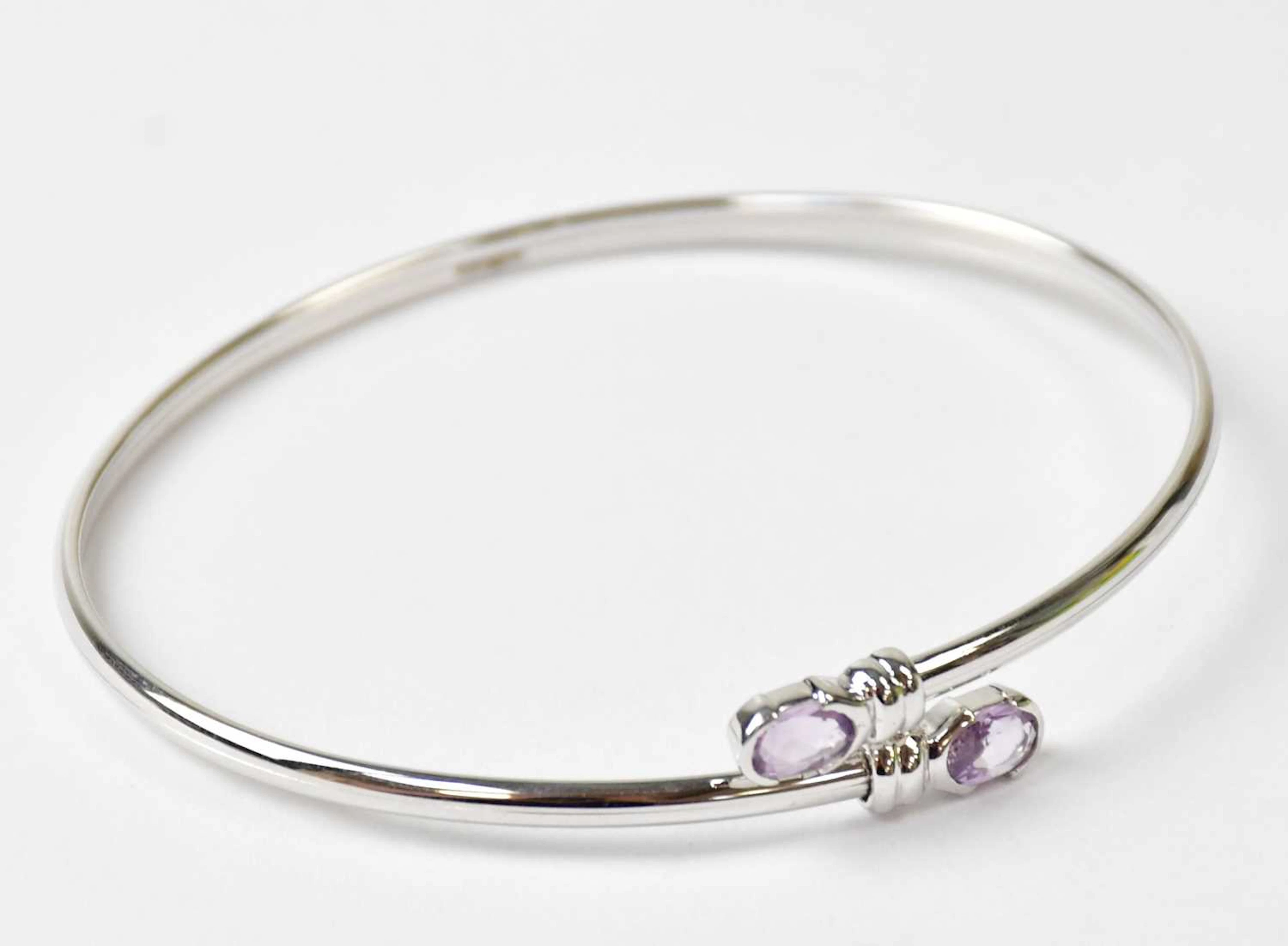 A 9ct white gold torc bangle set with an oval amethyst to each end