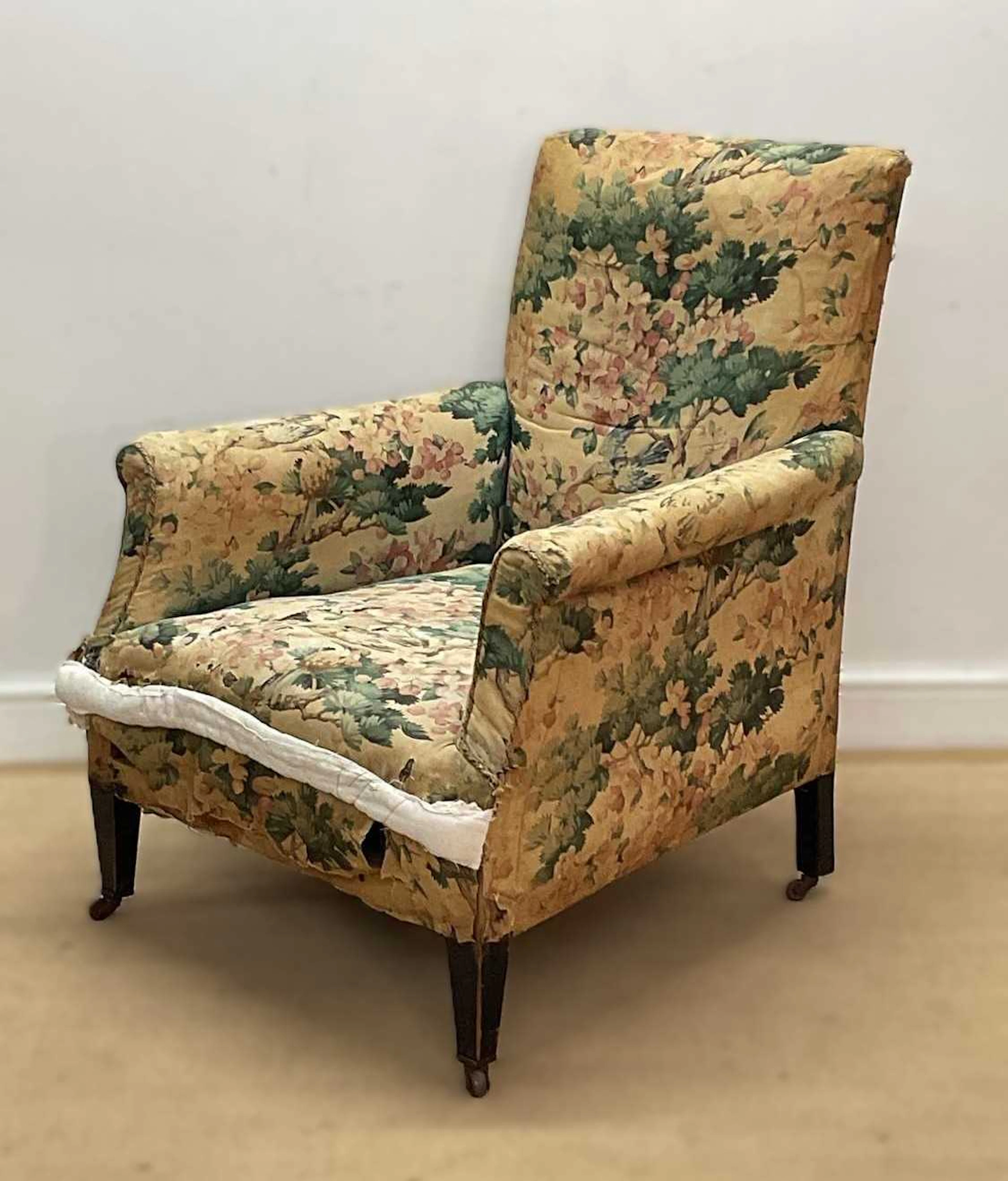 An early 20th century floral upholstered armchair with wooden legs and castors