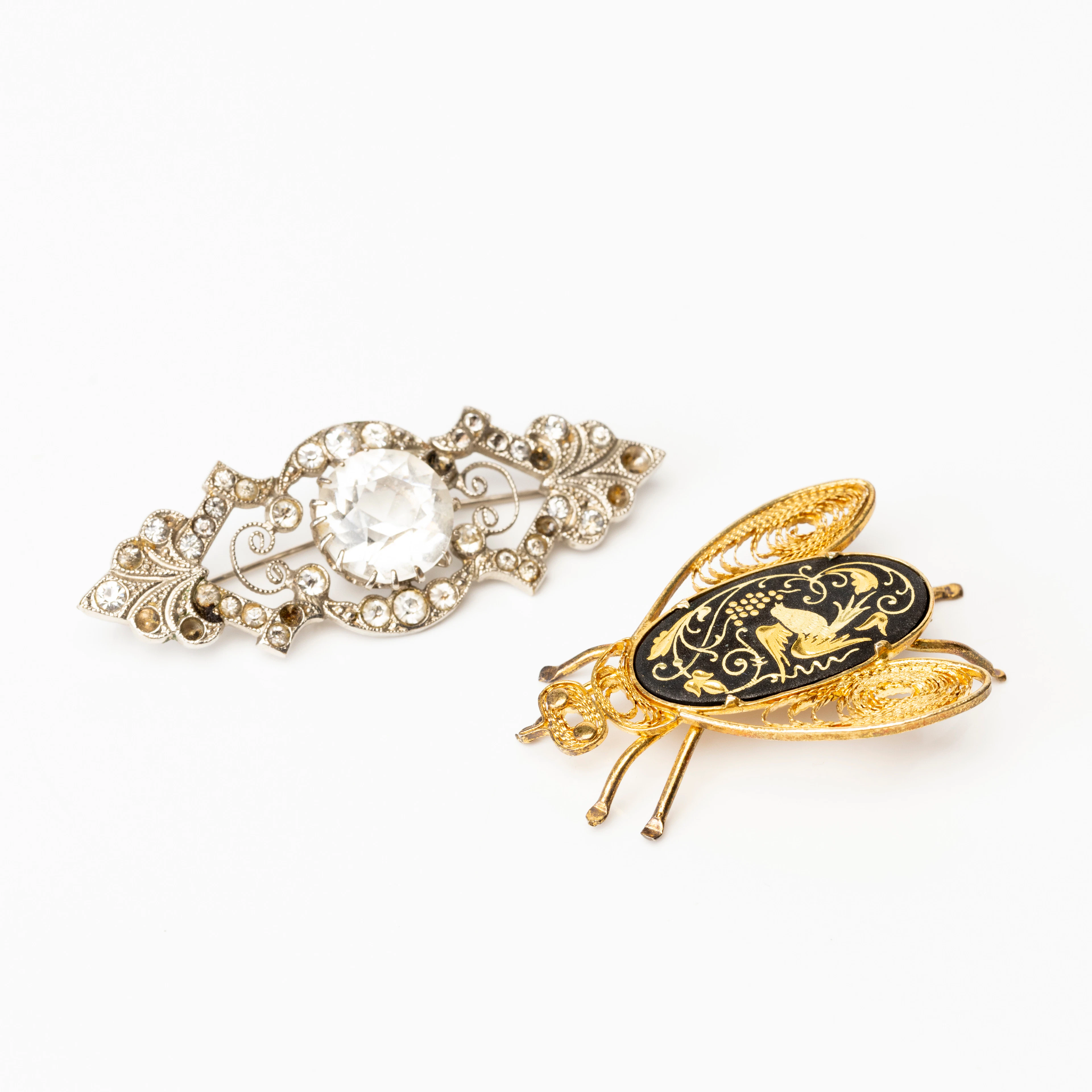 BROSCHER, 2 st, ljus metall samt paste, en med filigranarbete, 1900-tal.