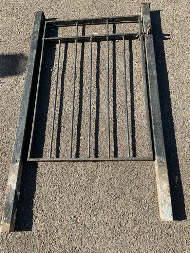 A wrought iron garden gate complete with two square capped gateposts