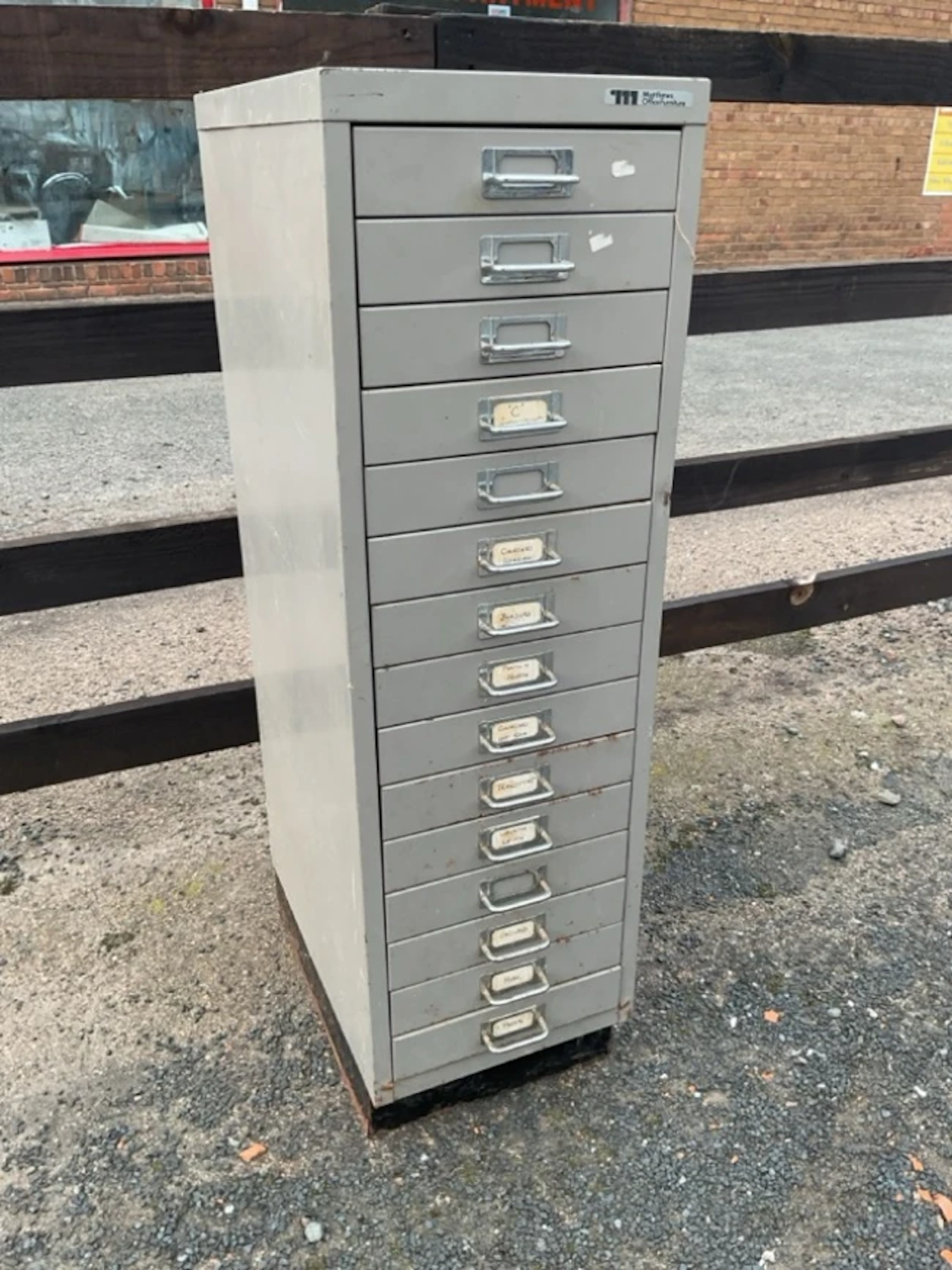A metal cabinet of fifteen small drawers with chromed tubular label