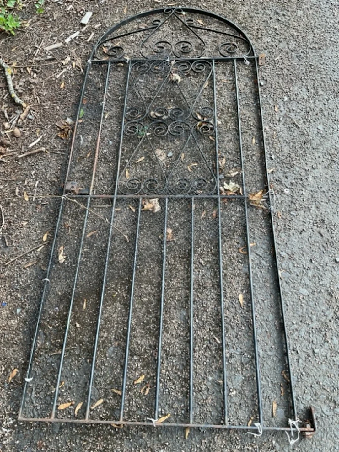 An arched wrought iron garden gate with spindles, having scrolled
