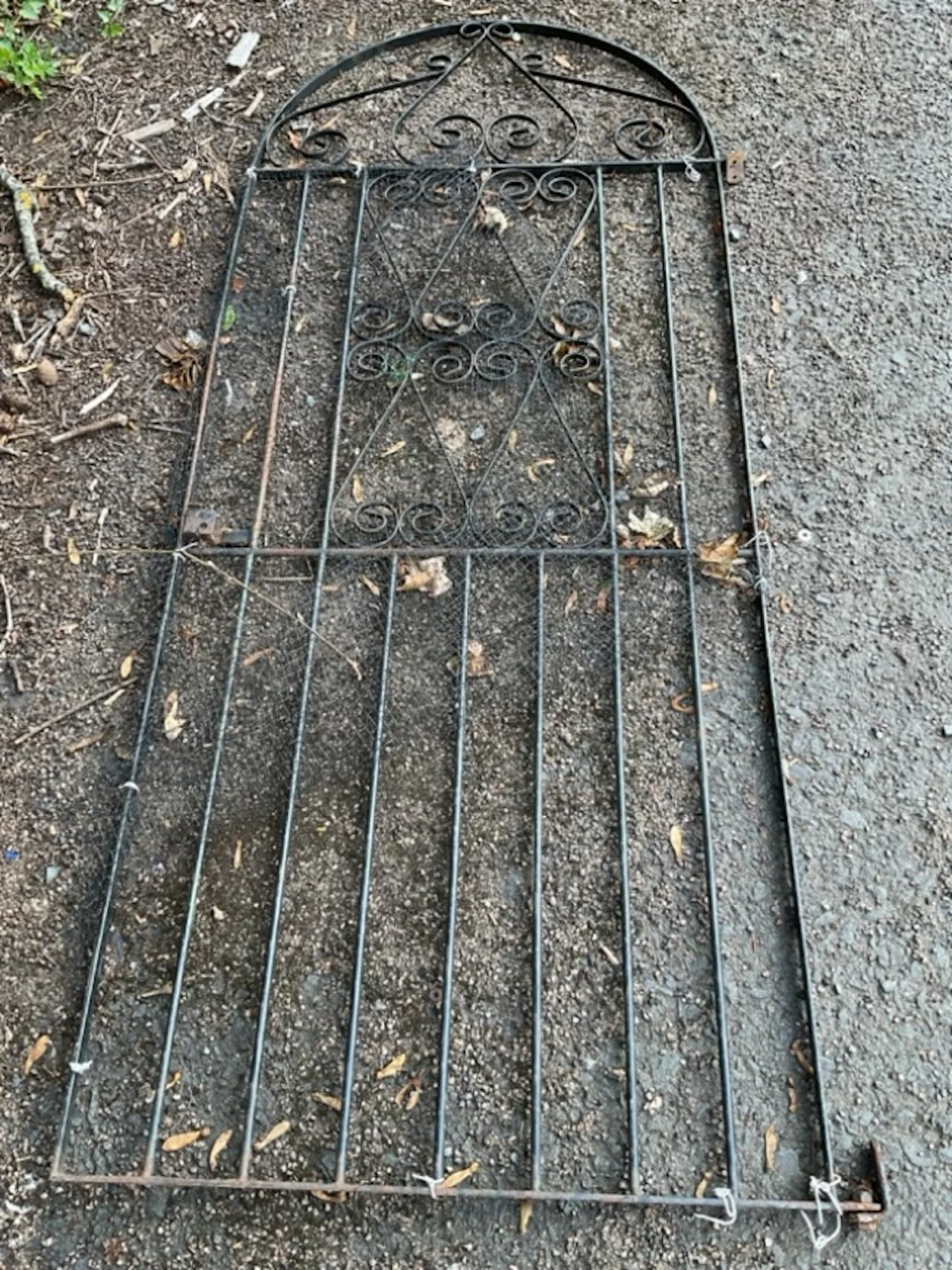 An arched wrought iron garden gate with spindles, having scrolled