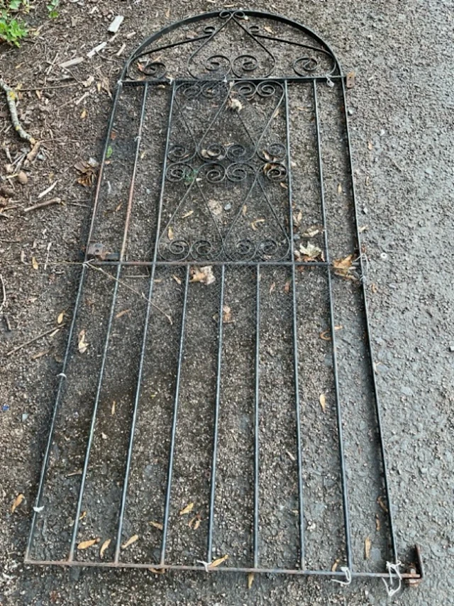 An arched wrought iron garden gate with spindles, having scrolled