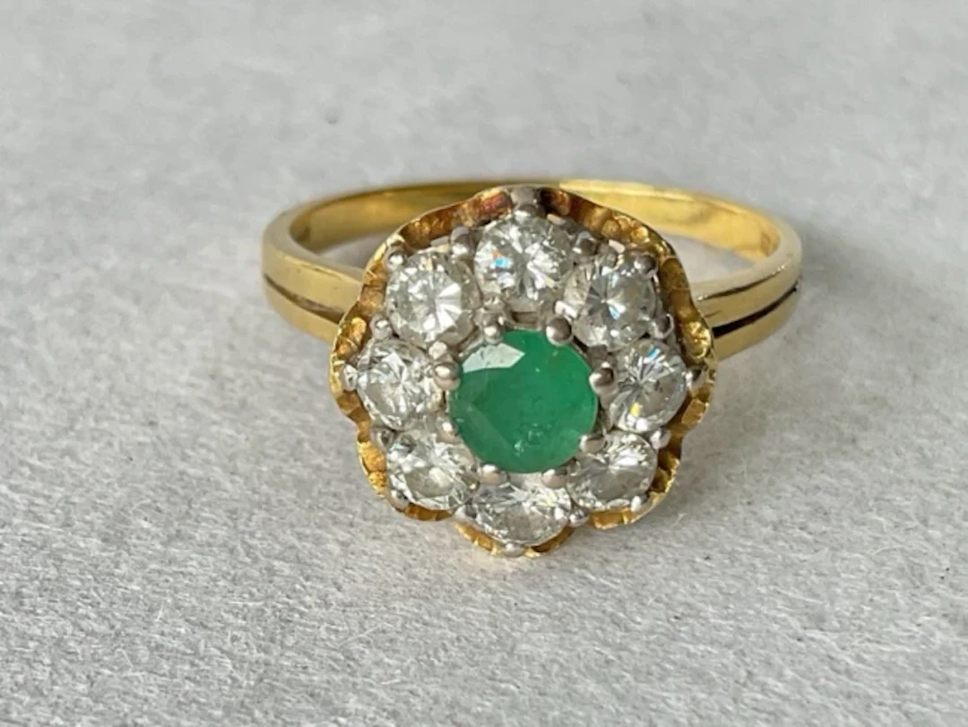 An 18ct gold cluster ring with central claw set emerald framed by