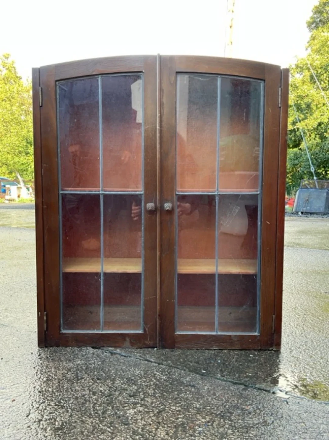 An oak cabinet with arched leaded glass doors enclosing adjustable