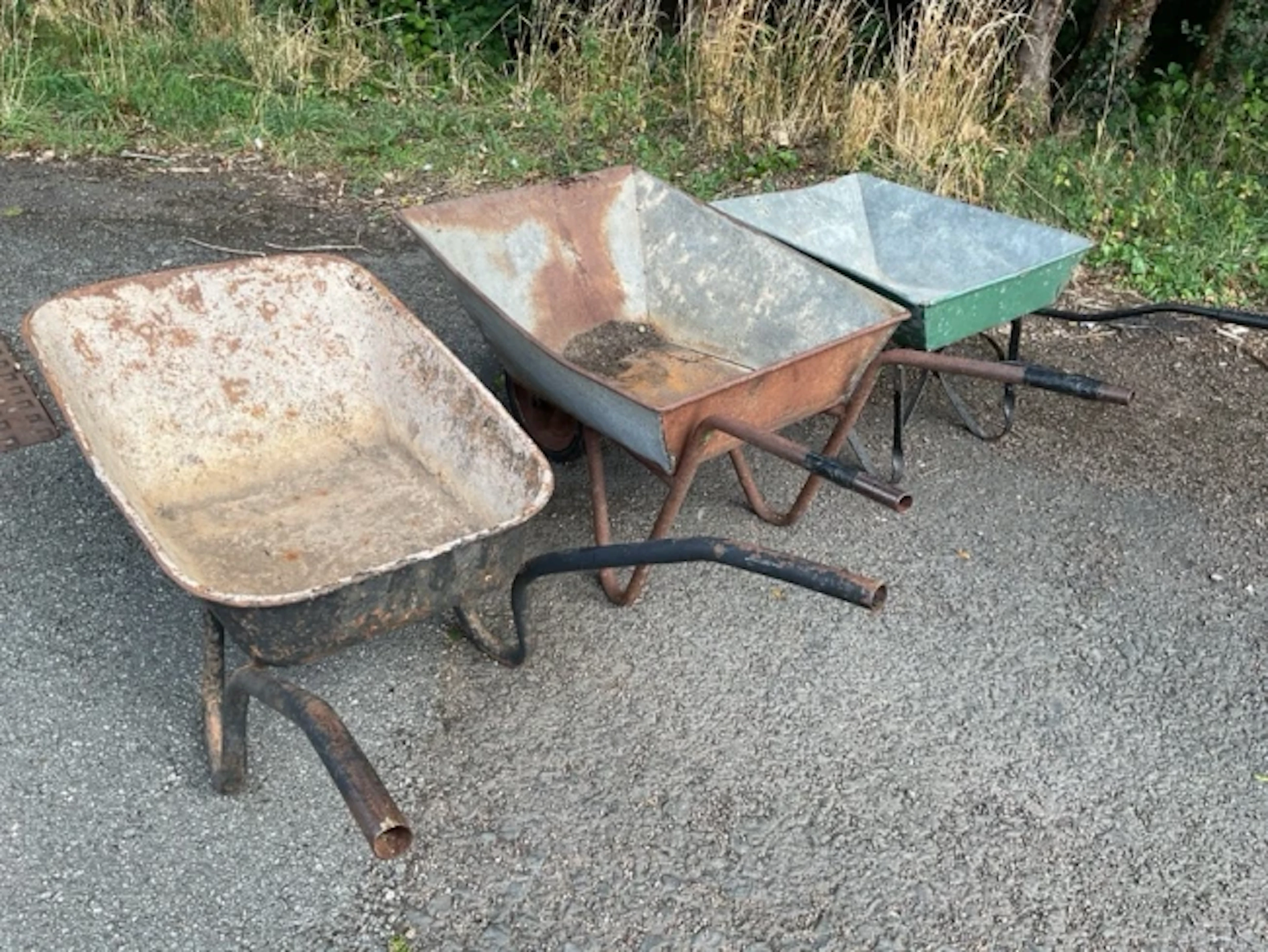 Two old galvanised wheelbarrows; and another metal with rolled rim