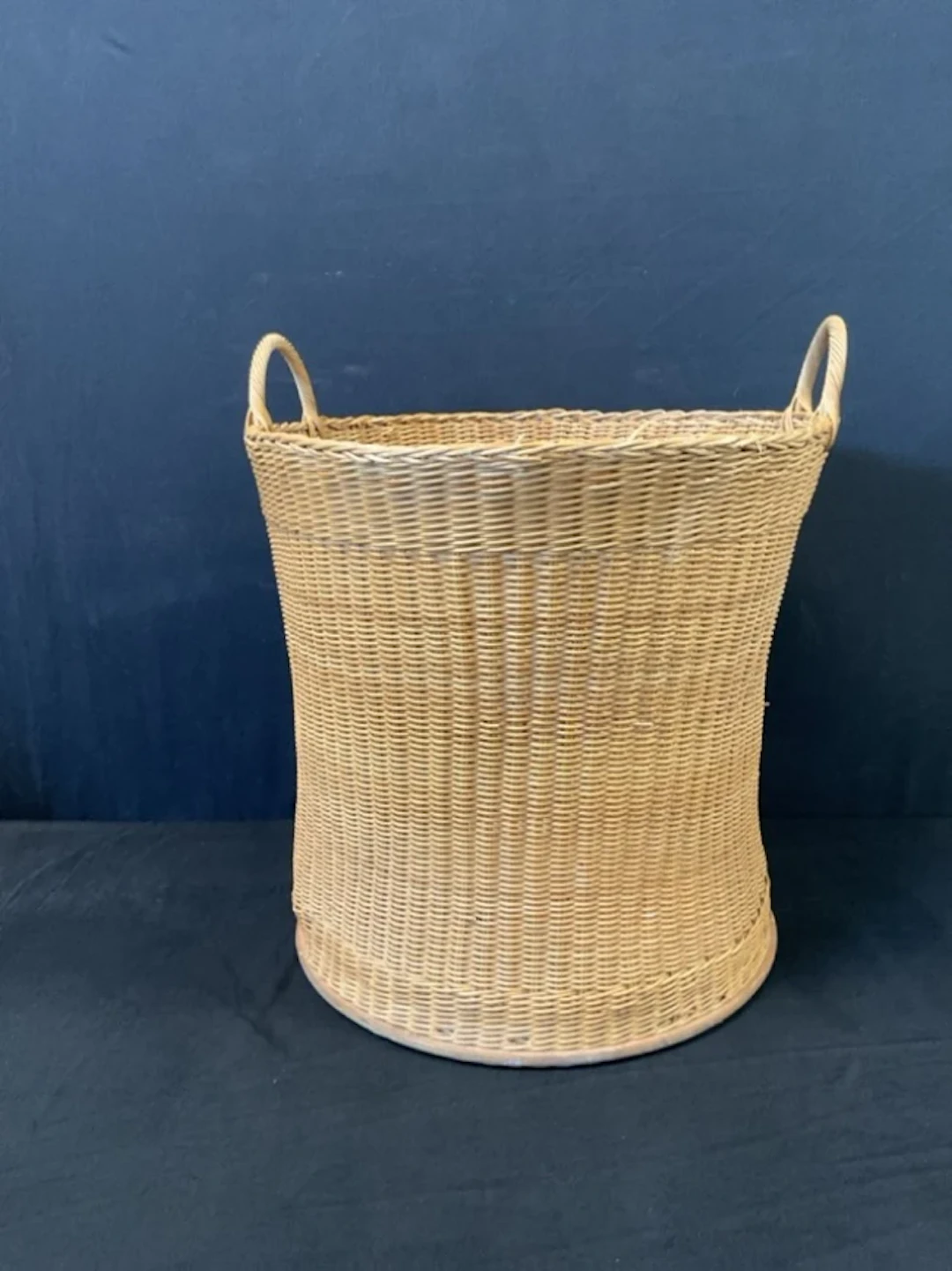 A waisted cylindrical cane log basket with plywood base and twin handles.