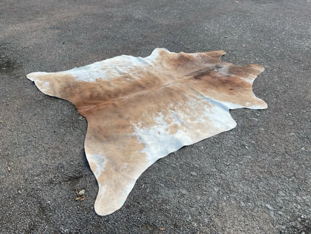 A large cowhide rug with brown and white speckled hair. (86in x 83in)