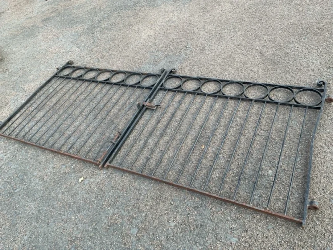 A pair of wrought iron driveway gates with scrolled finials to cornerposts