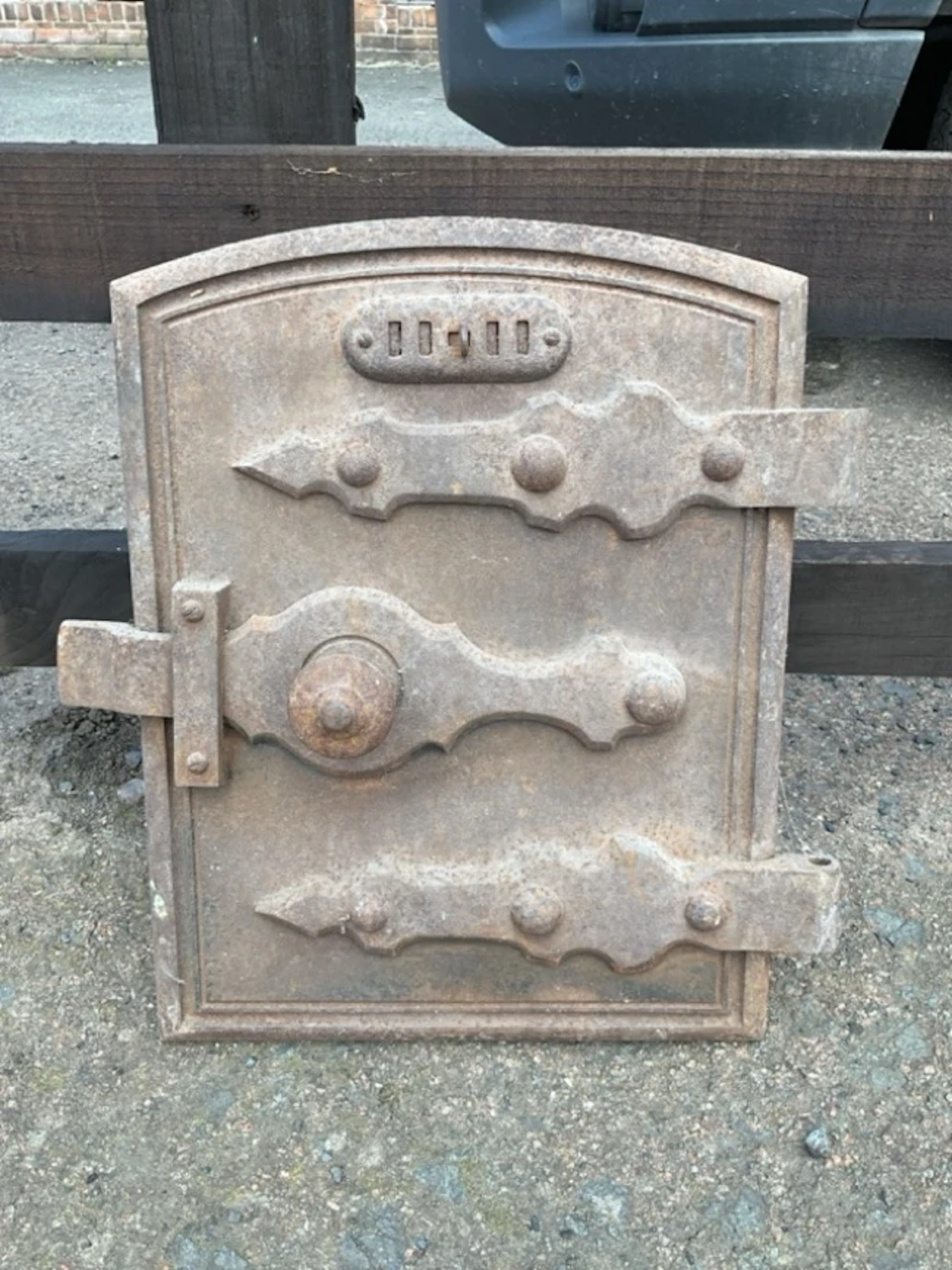 A C19th arched cast iron range door with sliding vent, shaped strap
