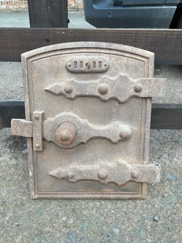 A C19th arched cast iron range door with sliding vent, shaped strap