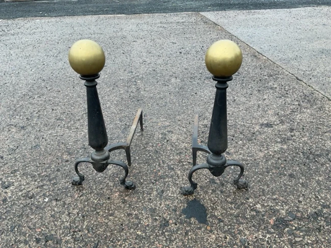 A pair of metal firedogs with brass ball finials to tapering columns