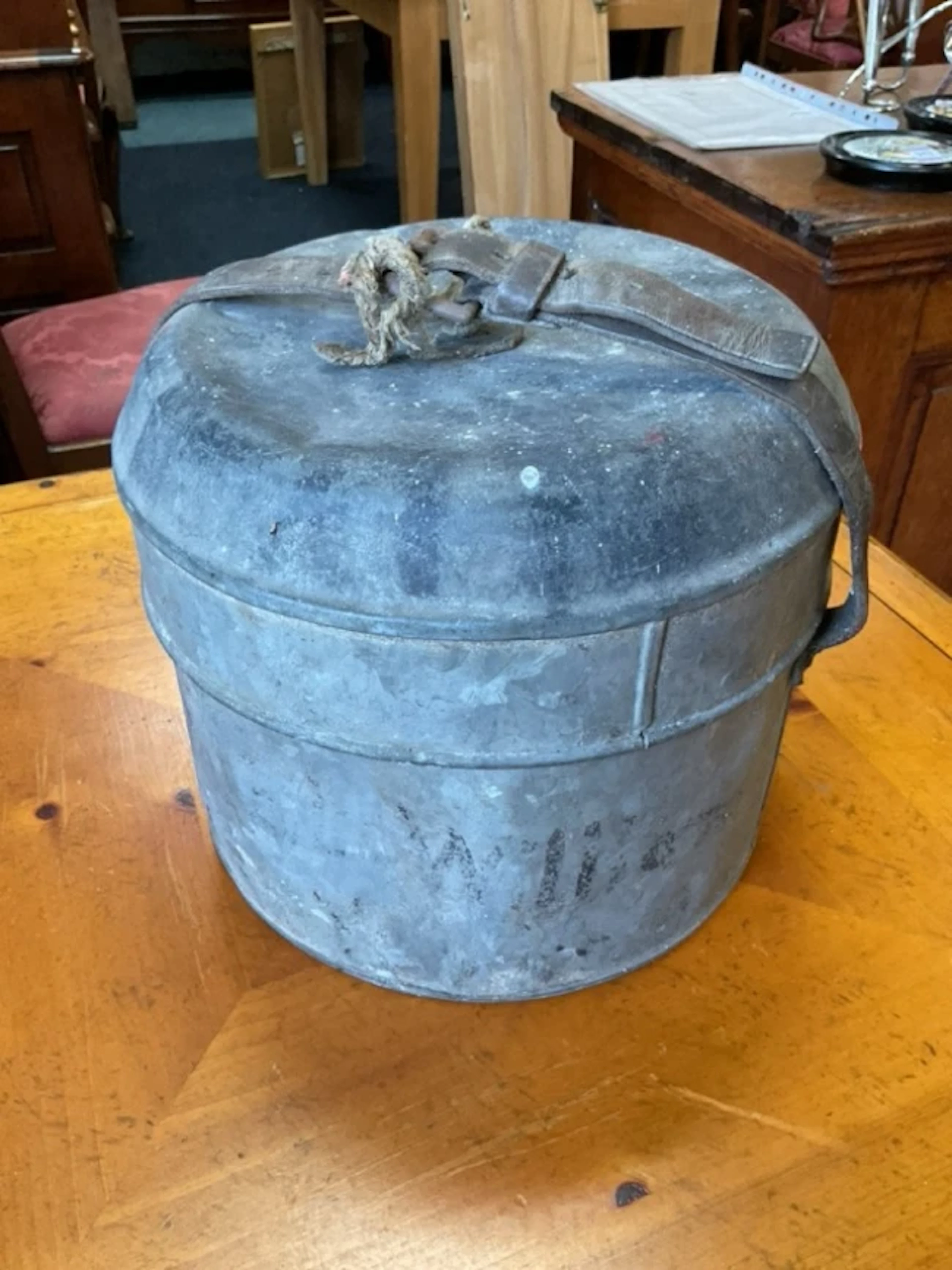 A galvanised metal doomed top hatbox with leather strap with faded