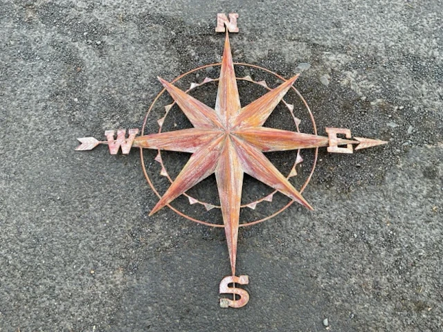A wall-hanging painted metal compass point panel, with central star