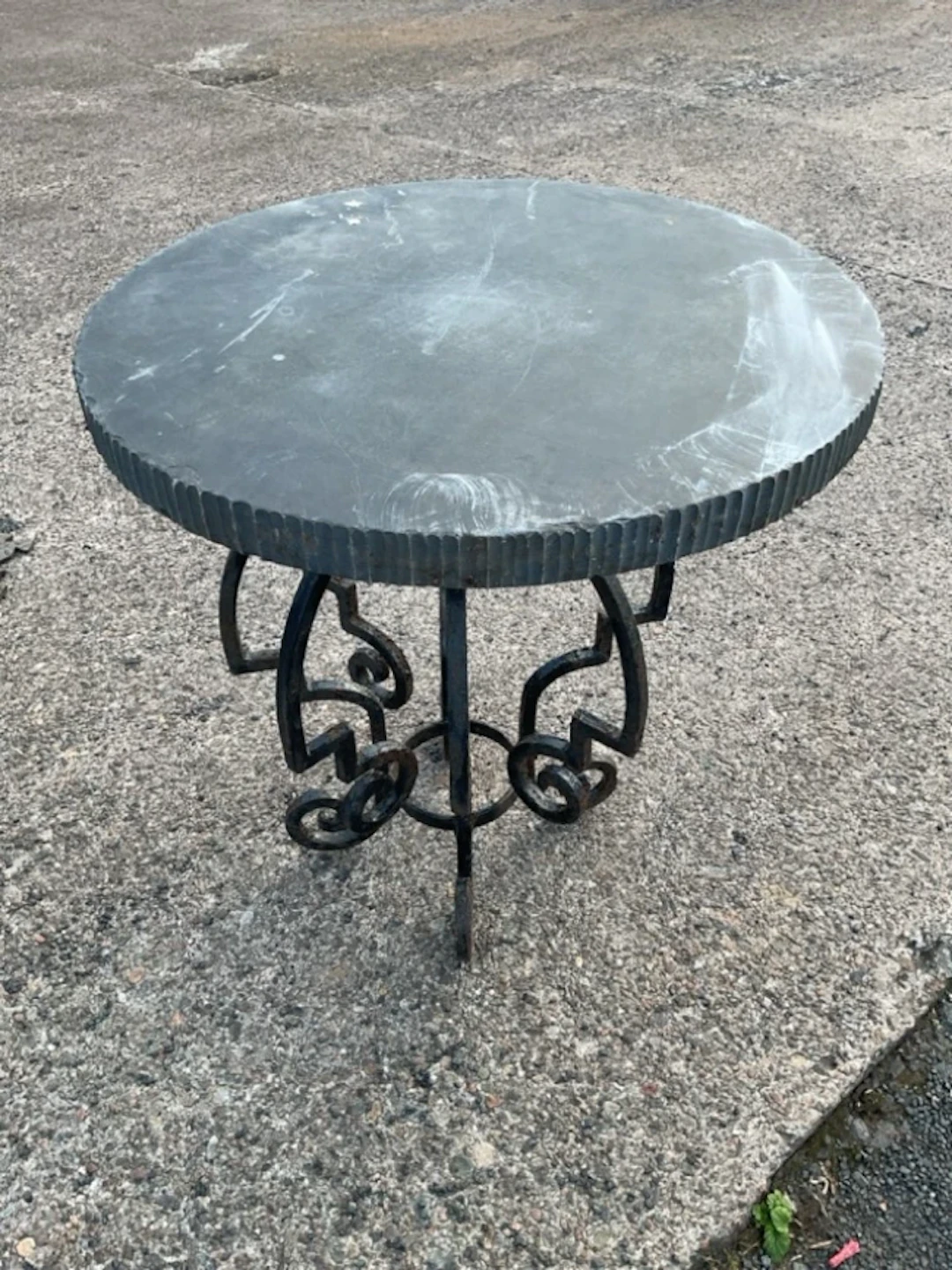 A garden table with wrought iron scrolled base having circular associated