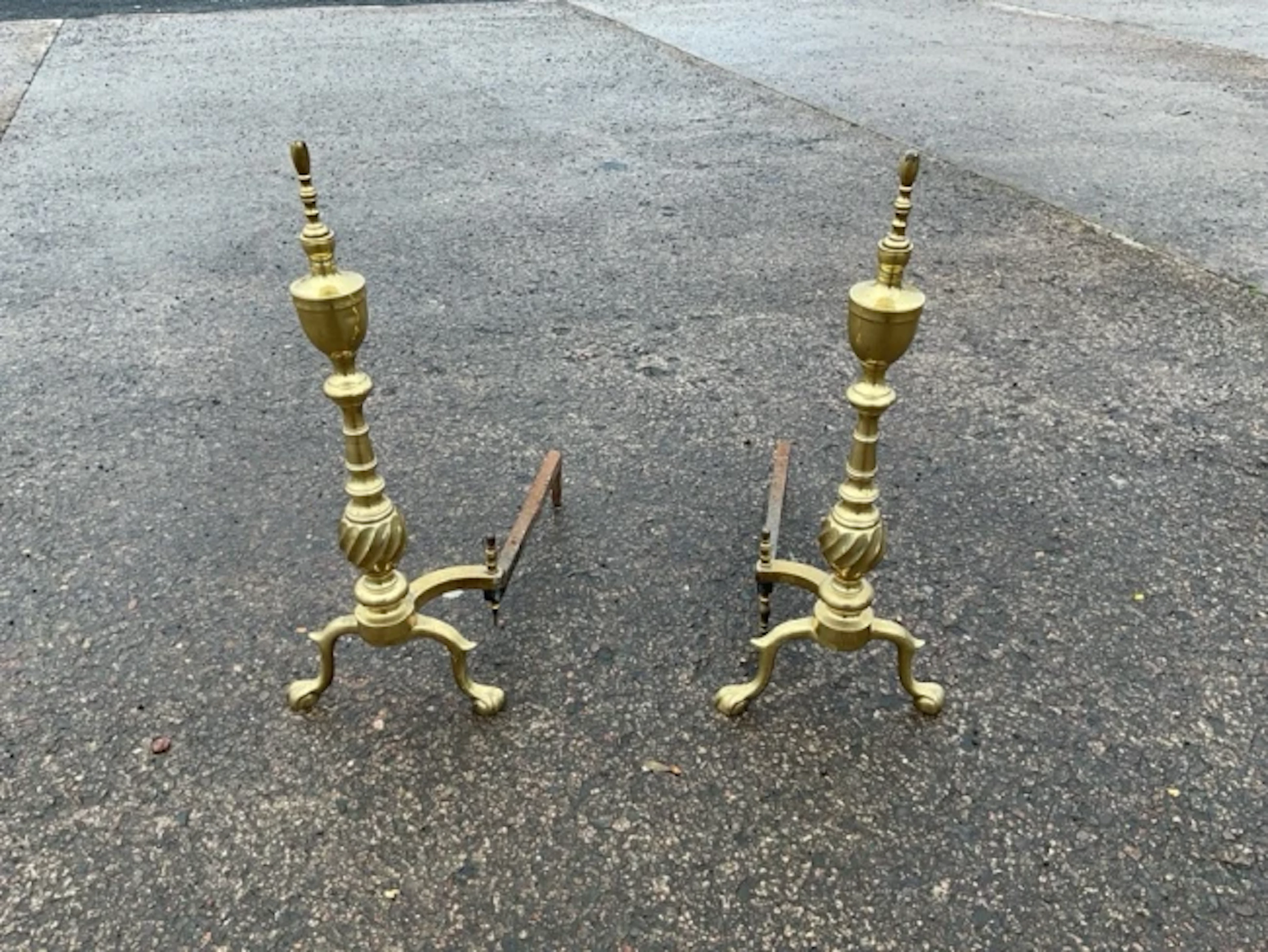 A pair of brass firedogs with tapering urn shaped twisted columns