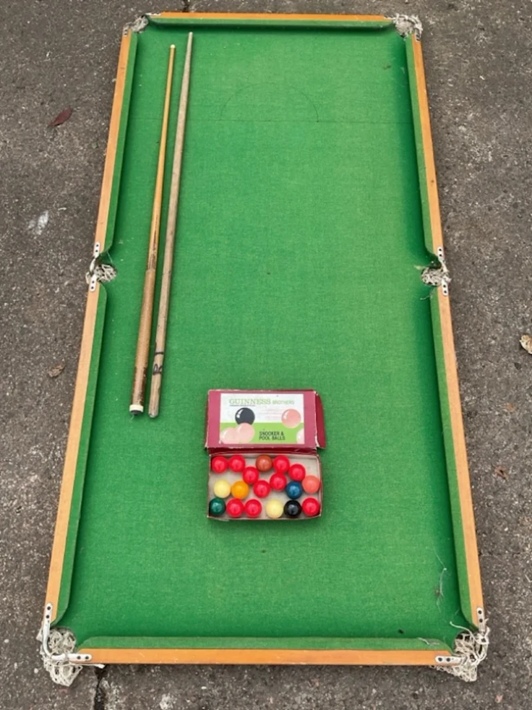 A tabletop snooker table with two cues and a boxed set of Guinness