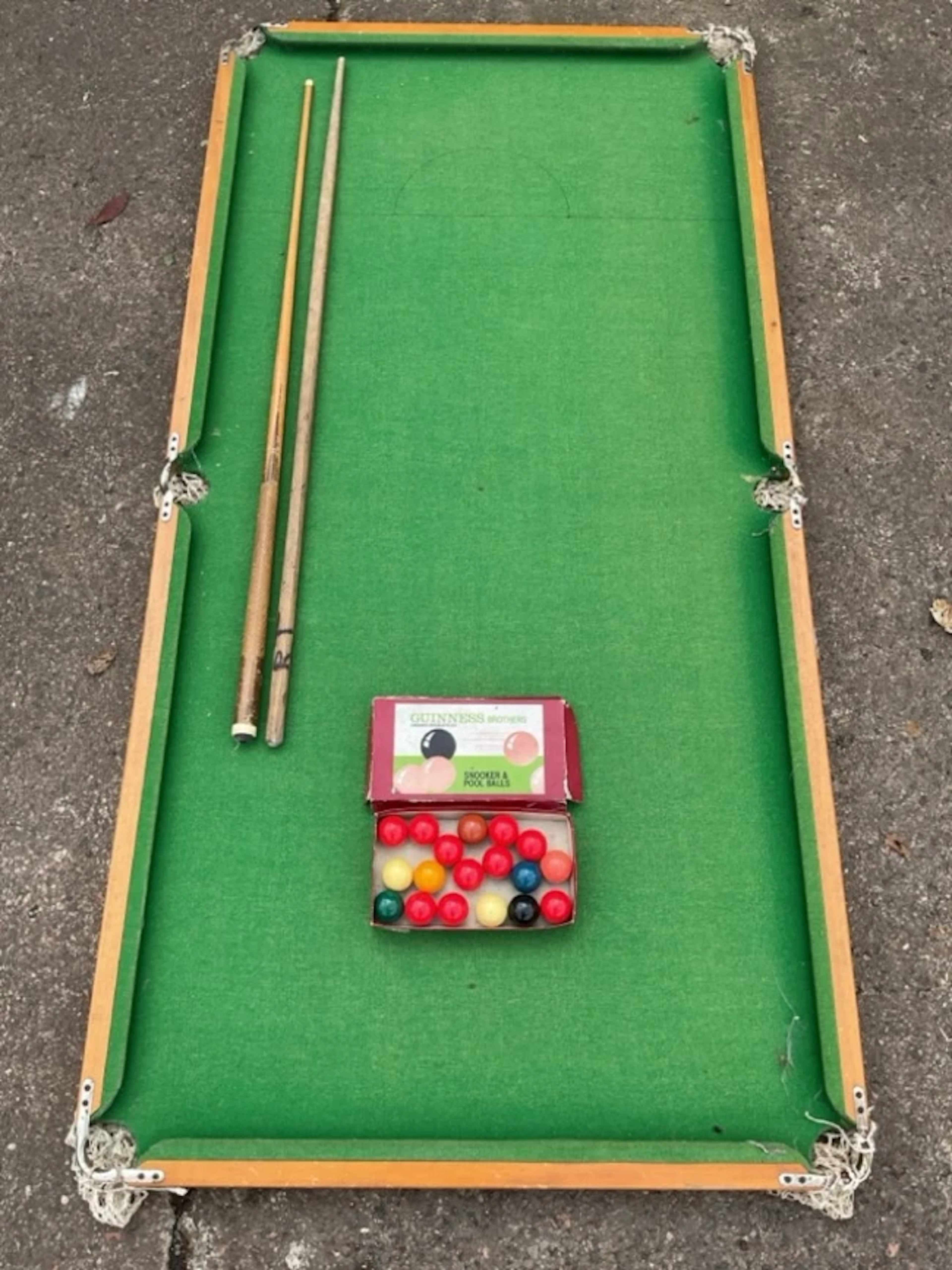 A tabletop snooker table with two cues and a boxed set of Guinness