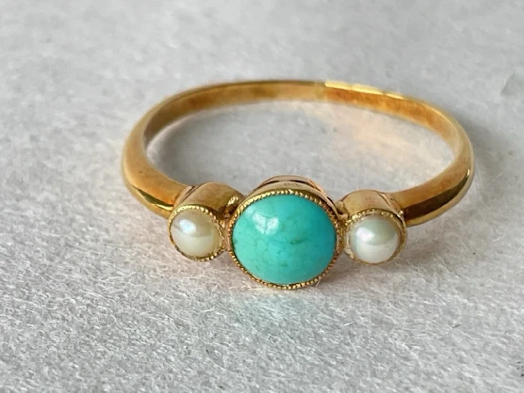 An 18ct gold ring with central cabochon turquoise flanked by two pearls