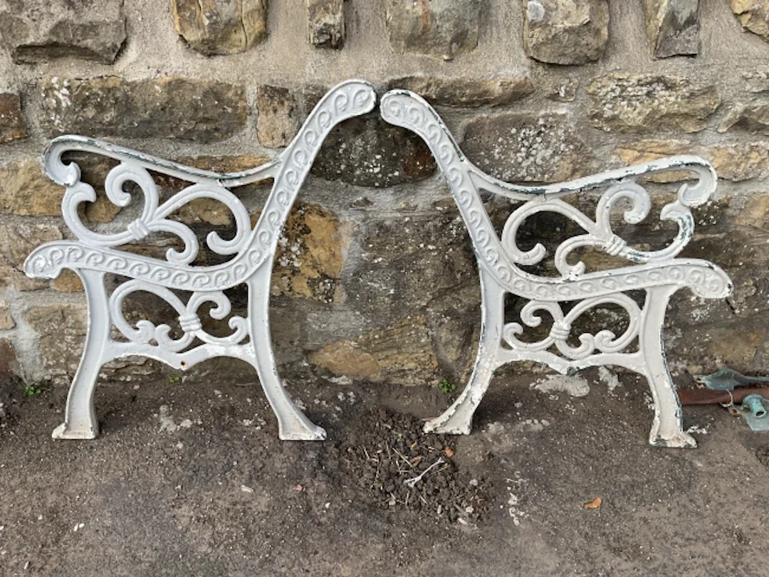A pair of painted cast iron garden bench ends with scrolled arms and