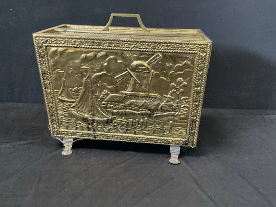 A rectangular brass magazine rack with embossed Dutch canal scene